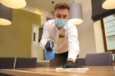 Photo of Waiter cleaning table with rag and detergent in restaurant. Surface treatment during coronavirus quarantine