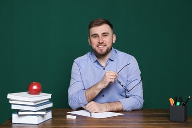 Portrait of young teacher at table against green background