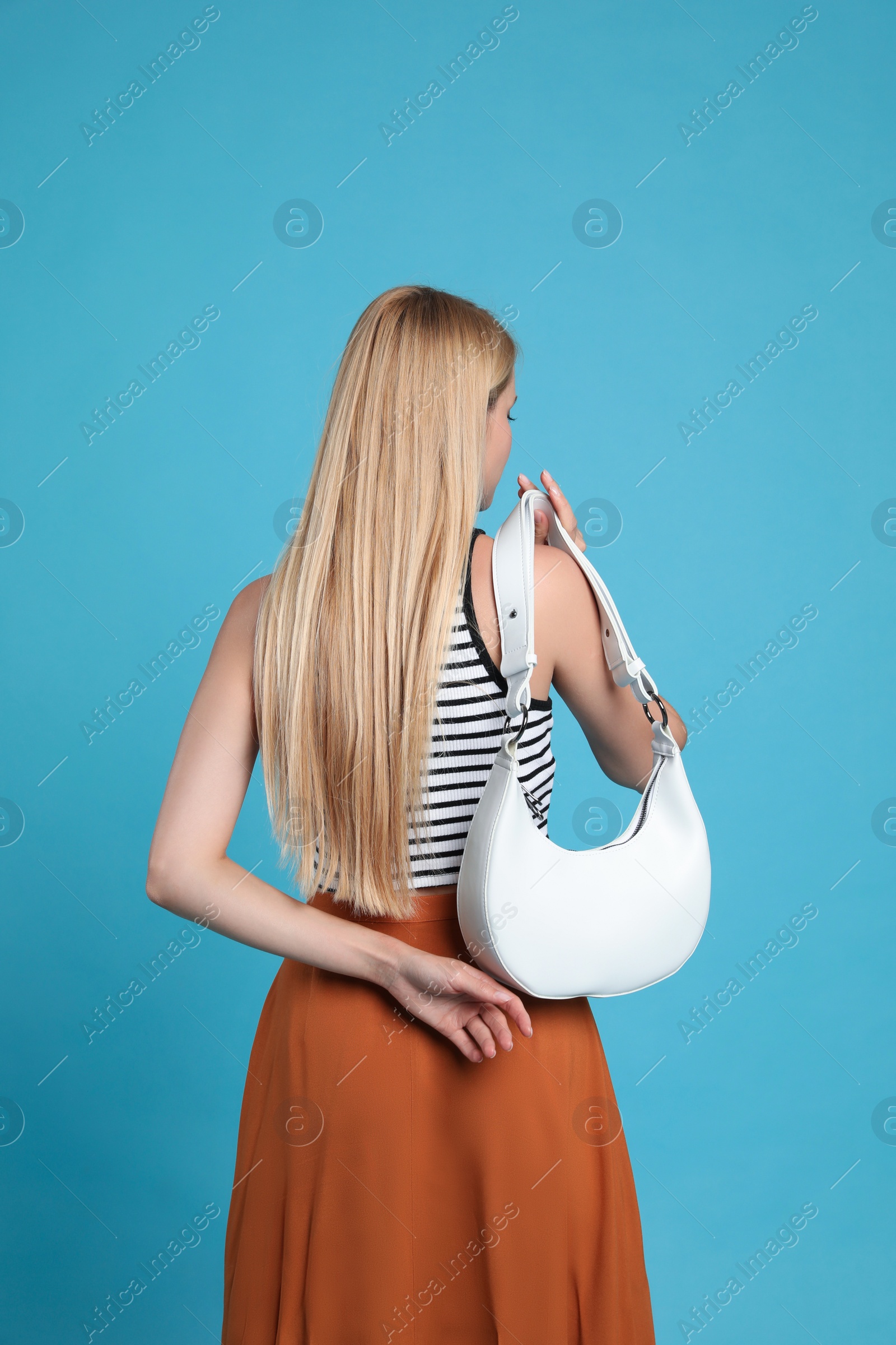 Photo of Beautiful stylish woman with trendy baguette bag on turquoise background, back view