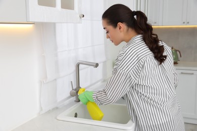 Photo of Woman with spray bottle cleaning water tap in kitchen