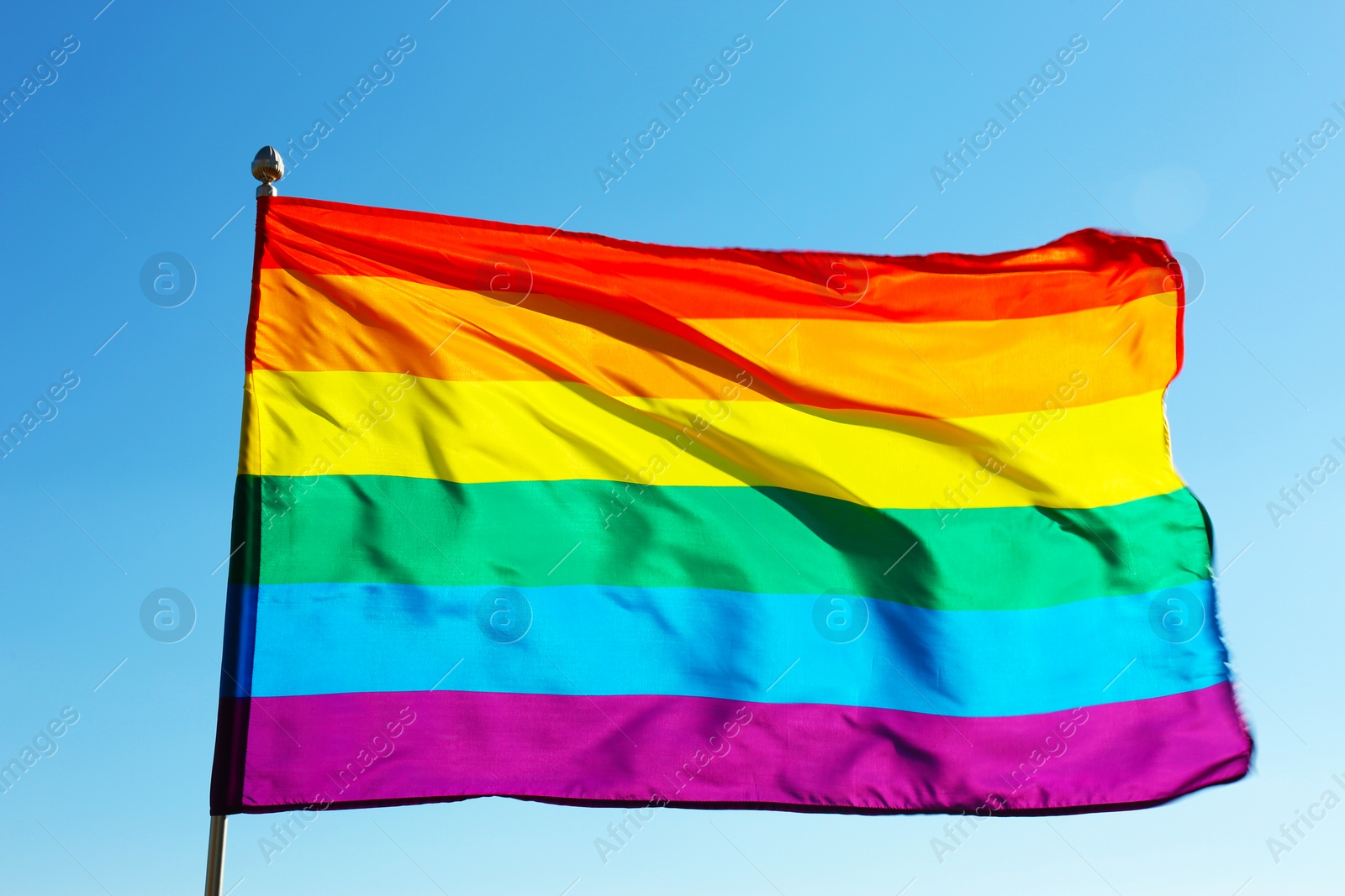 Photo of Rainbow LGBT flag fluttering on blue sky background. Gay rights movement