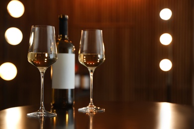 Bottle and glasses of wine on table against blurred background. Space for text