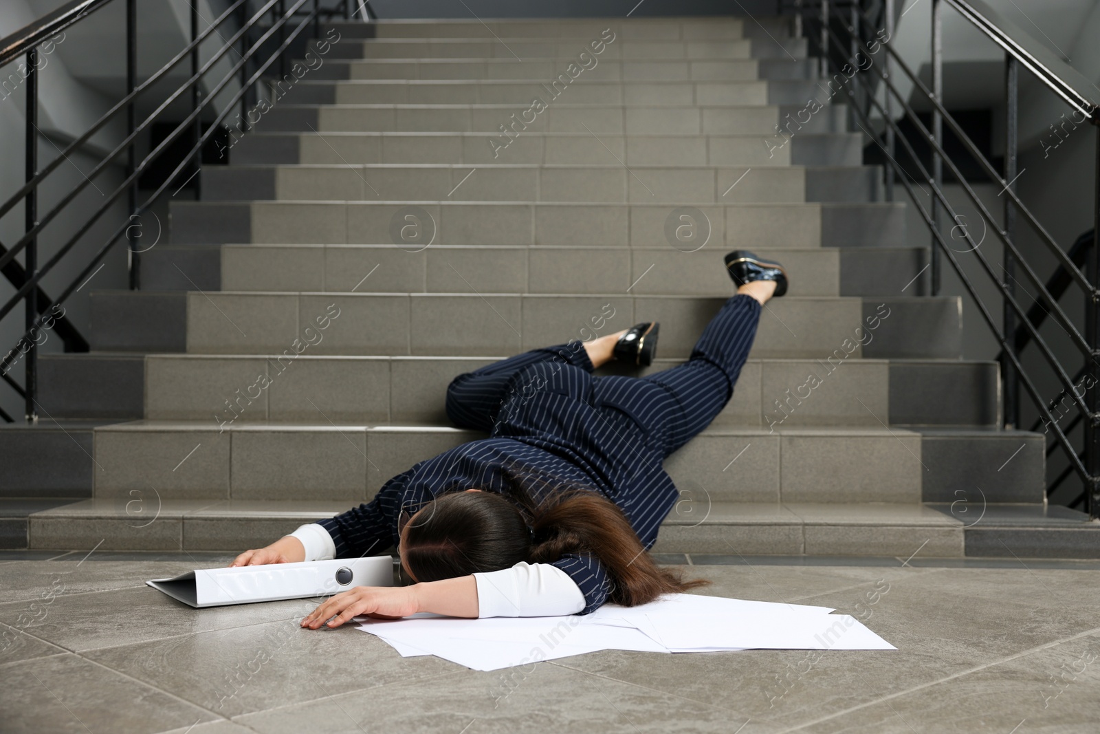 Photo of Unconscious woman with scattered folder and papers lying on floor after falling down stairs indoors