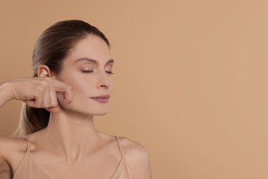 Woman massaging her face on beige background. Space for text