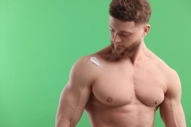 Photo of Handsome man with moisturizing cream on his shoulder against green background, space for text