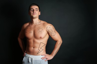 Image of Handsome man with beautiful tattoo sketches on black background. Space for text