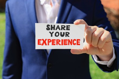 Photo of Man holding card with phrase Share Your Experience outdoors, closeup