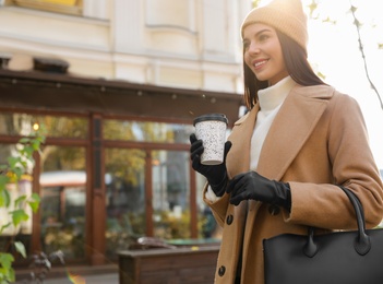Photo of Beautiful young woman with stylish leather gloves and cup of coffee on city street
