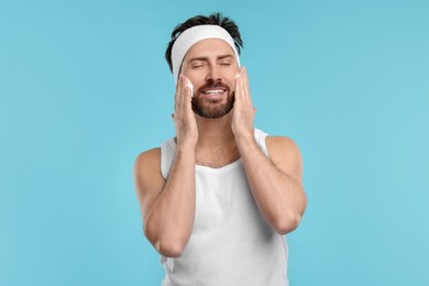 Photo of Man with headband washing his face on light blue background