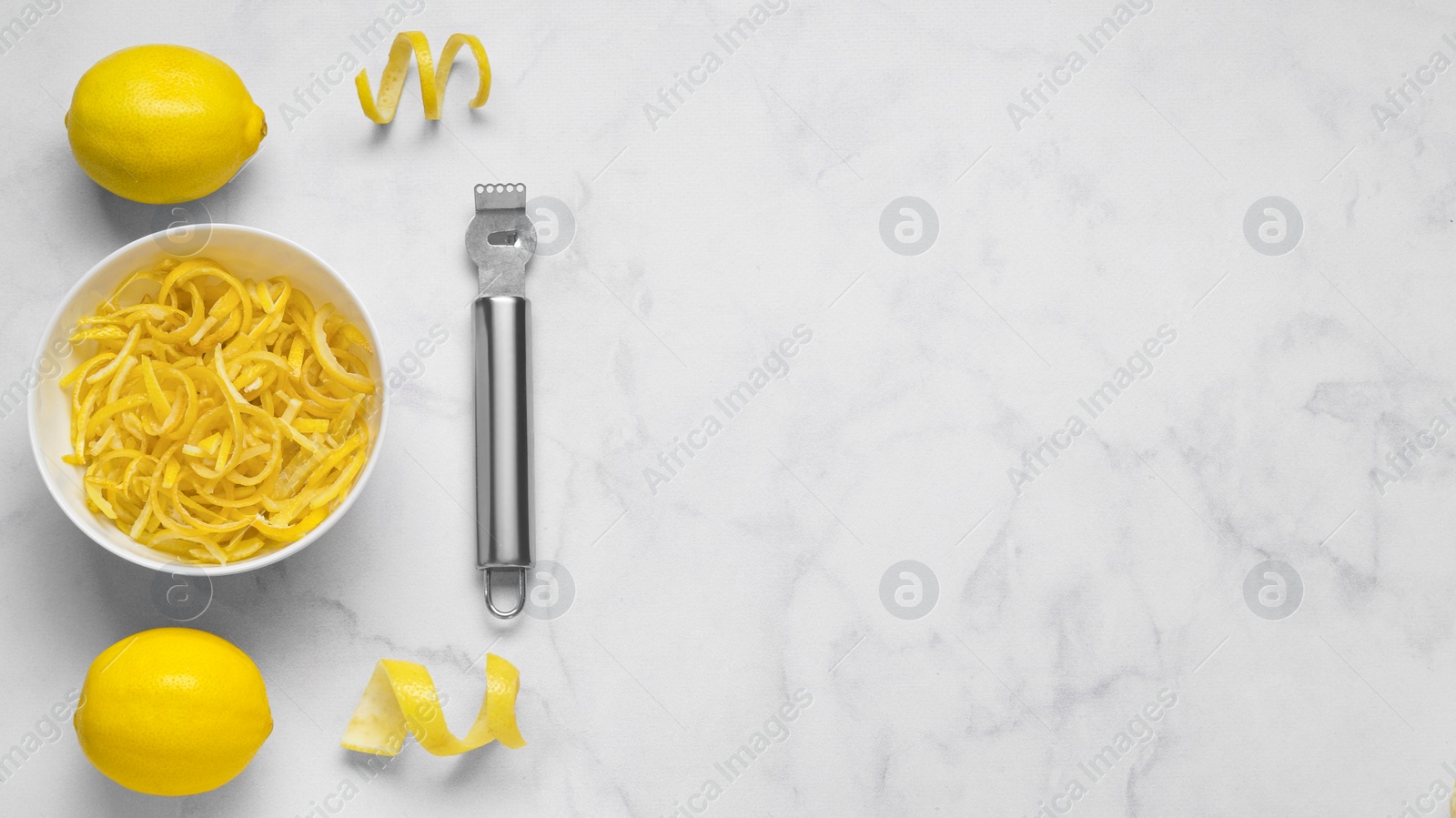 Photo of Bowl with peel pieces, fresh lemons and zester on white marble table, flat lay. Space for text