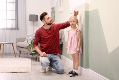 Young man measuring his daughter's height at home