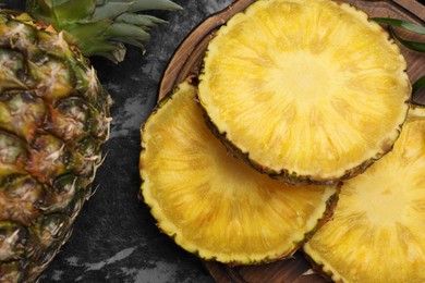 Photo of Slices of tasty ripe pineapple on black textured table, flat lay