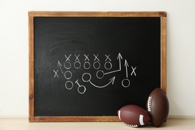 Rugby balls near chalkboard with football game scheme on table