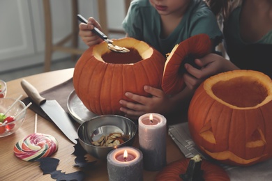Photo of Mother and daughter making pumpkin jack o'lantern at table, closeup. Halloween celebration