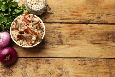 Photo of Tasty quinoa porridge with fried bacon, mushrooms in bowl on wooden table, flat lay. Space for text