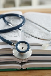 One new medical stethoscope and books on wooden table, closeup