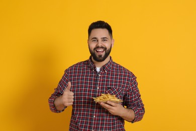 Young man with French fries on orange background