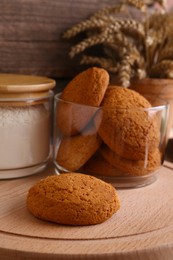 Photo of Cookies and jar of wheat flour on wooden board, closeup view