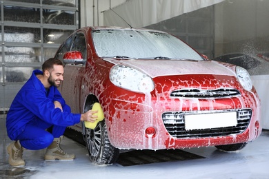 Young worker cleaning automobile wheel at car wash