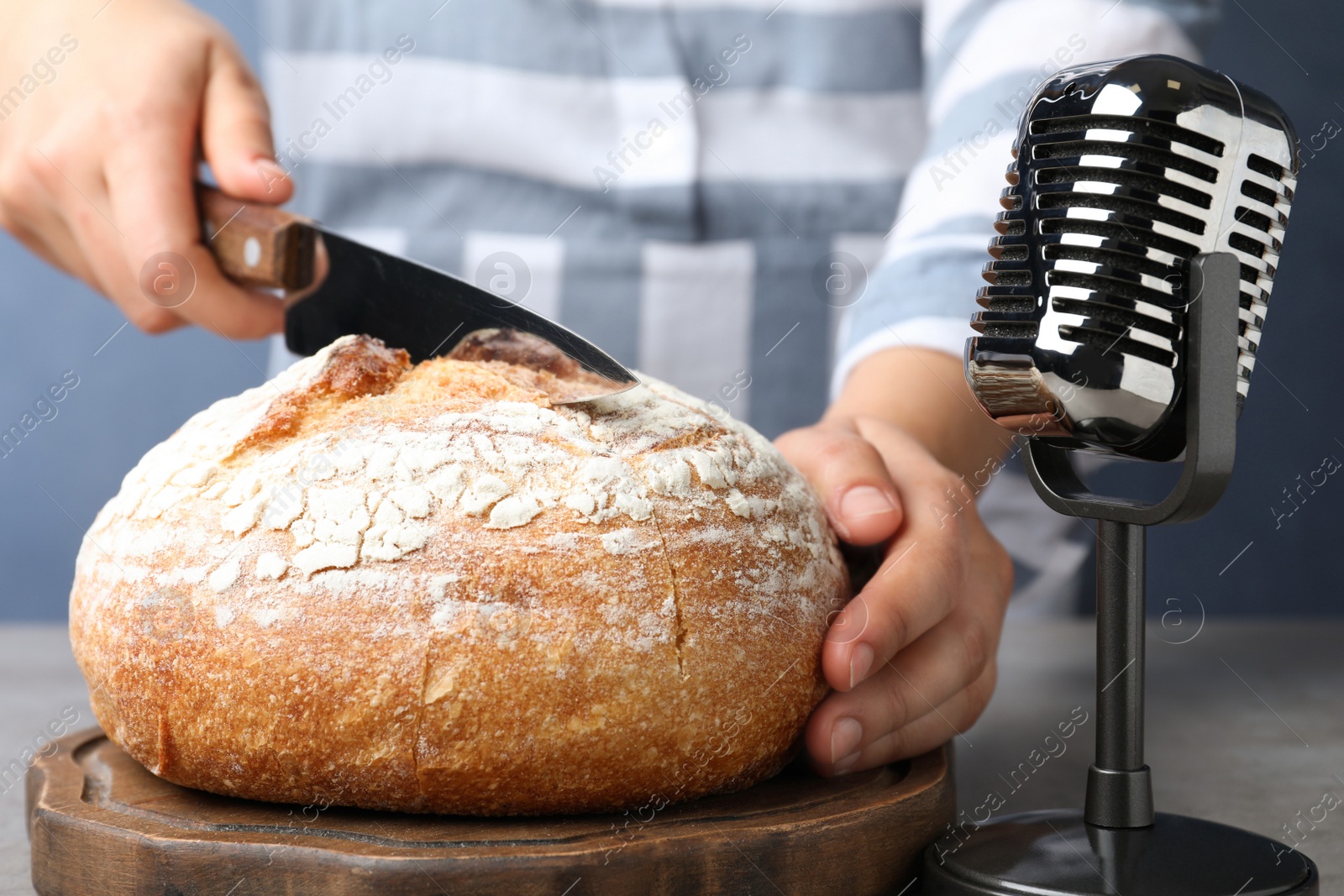 Photo of Woman making ASMR sounds with microphone and bread at grey table, closeup