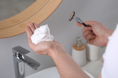 Photo of Man holding shaving foam and razor in bathroom, closeup
