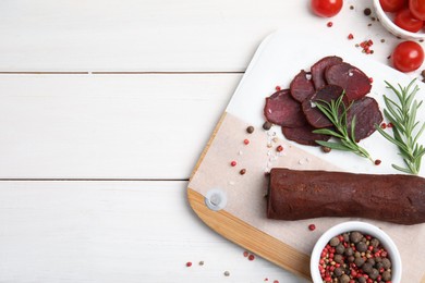 Photo of Delicious dry-cured beef basturma with rosemary and tomatoes on white wooden table, flat lay. Space for text