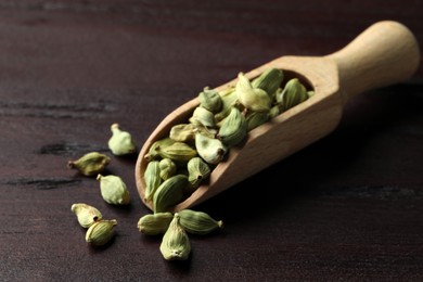 Photo of Scoop with dry cardamom pods on wooden table