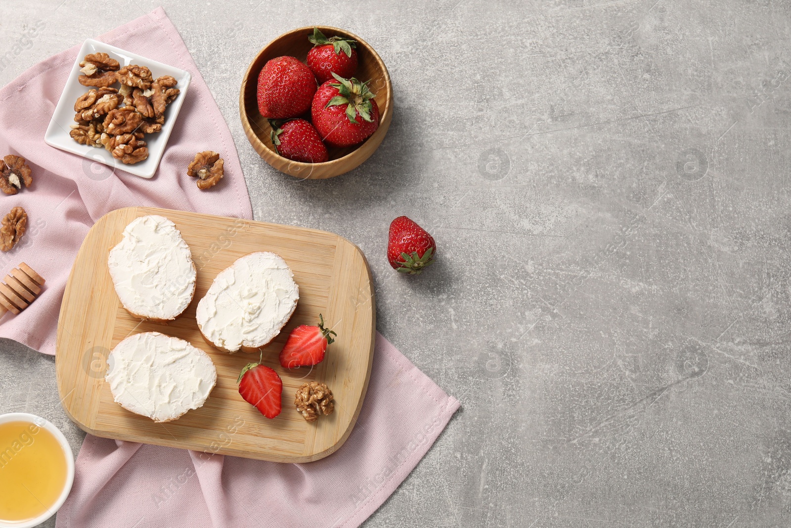 Photo of Delicious bruschettas with ricotta cheese, strawberries, walnuts and honey on grey textured table, flat lay. Space for text