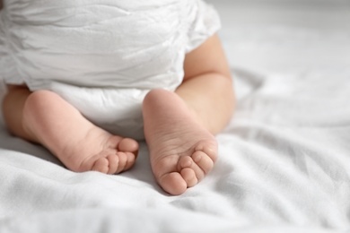 Cute little baby crawling on white bed sheet, closeup. Space for text