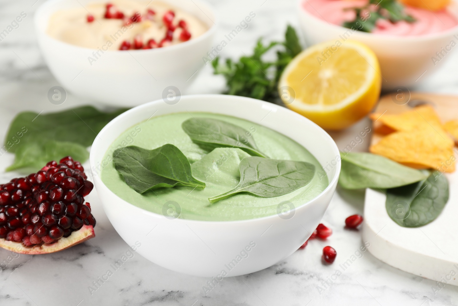 Photo of Bowl of delicious green hummus with spinach on white marble table