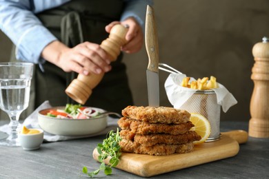 Photo of Tasty schnitzels served with knife, french fries and woman cooking salad at grey table, closeup