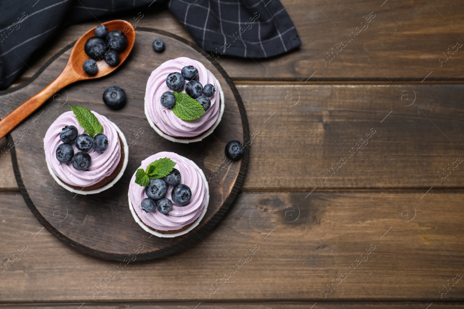 Photo of Sweet cupcakes with fresh blueberries on wooden table, flat lay. Space for text