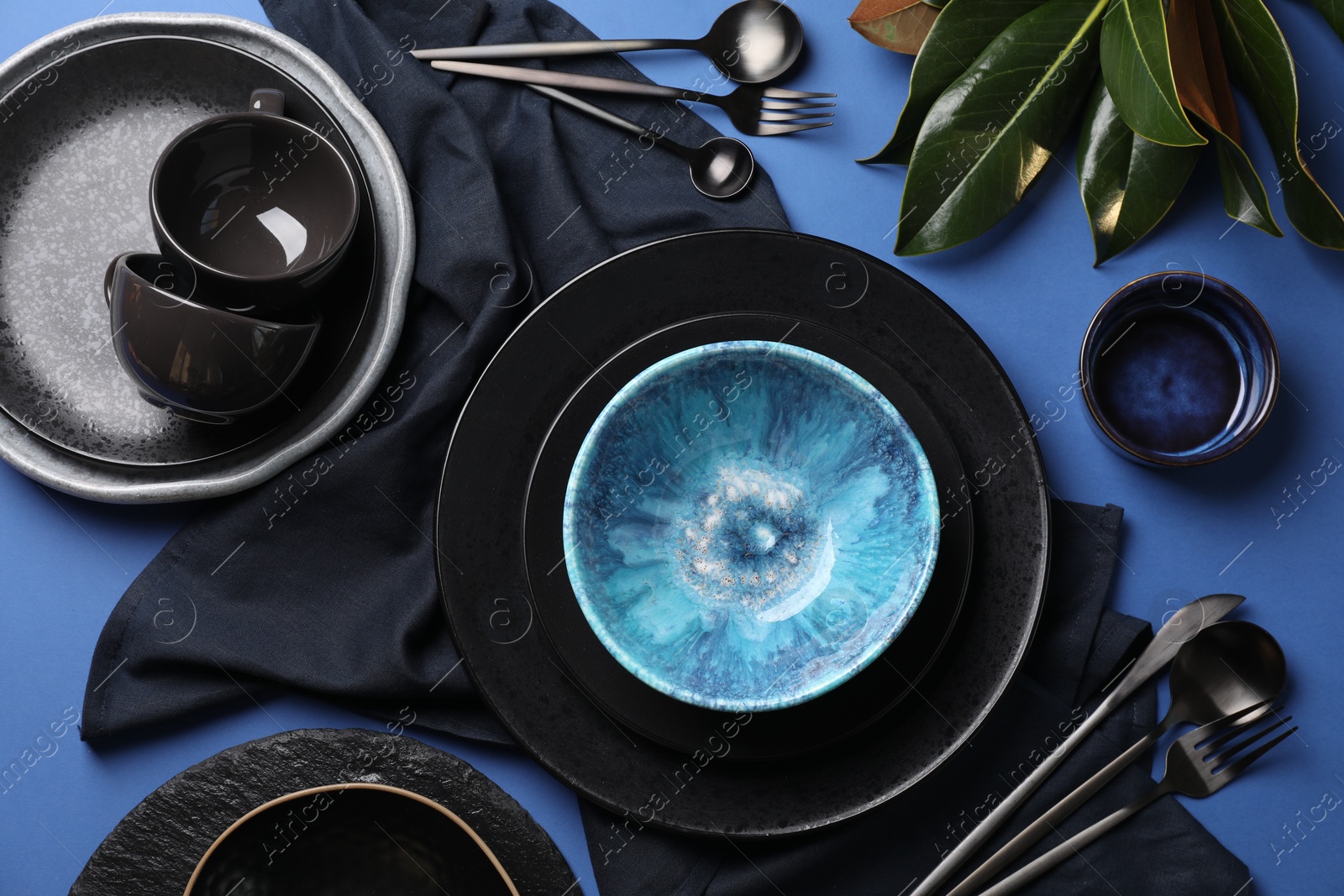 Photo of Stylish table setting. Dishware, cutlery and floral decor on blue background, flat lay