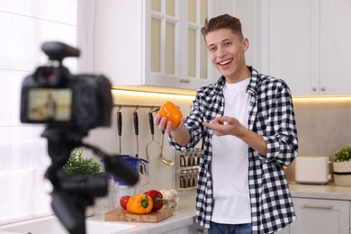 Photo of Smiling food blogger talking about bell pepper while recording video in kitchen