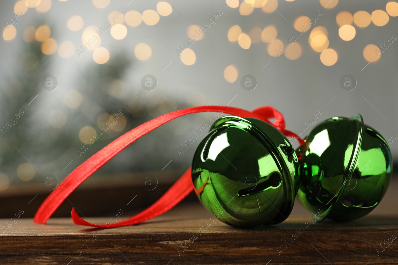 Photo of Green sleigh bells with red ribbon on wooden table, closeup