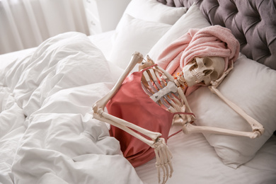 Photo of Human skeleton in silk pajamas and towel lying on bed indoors