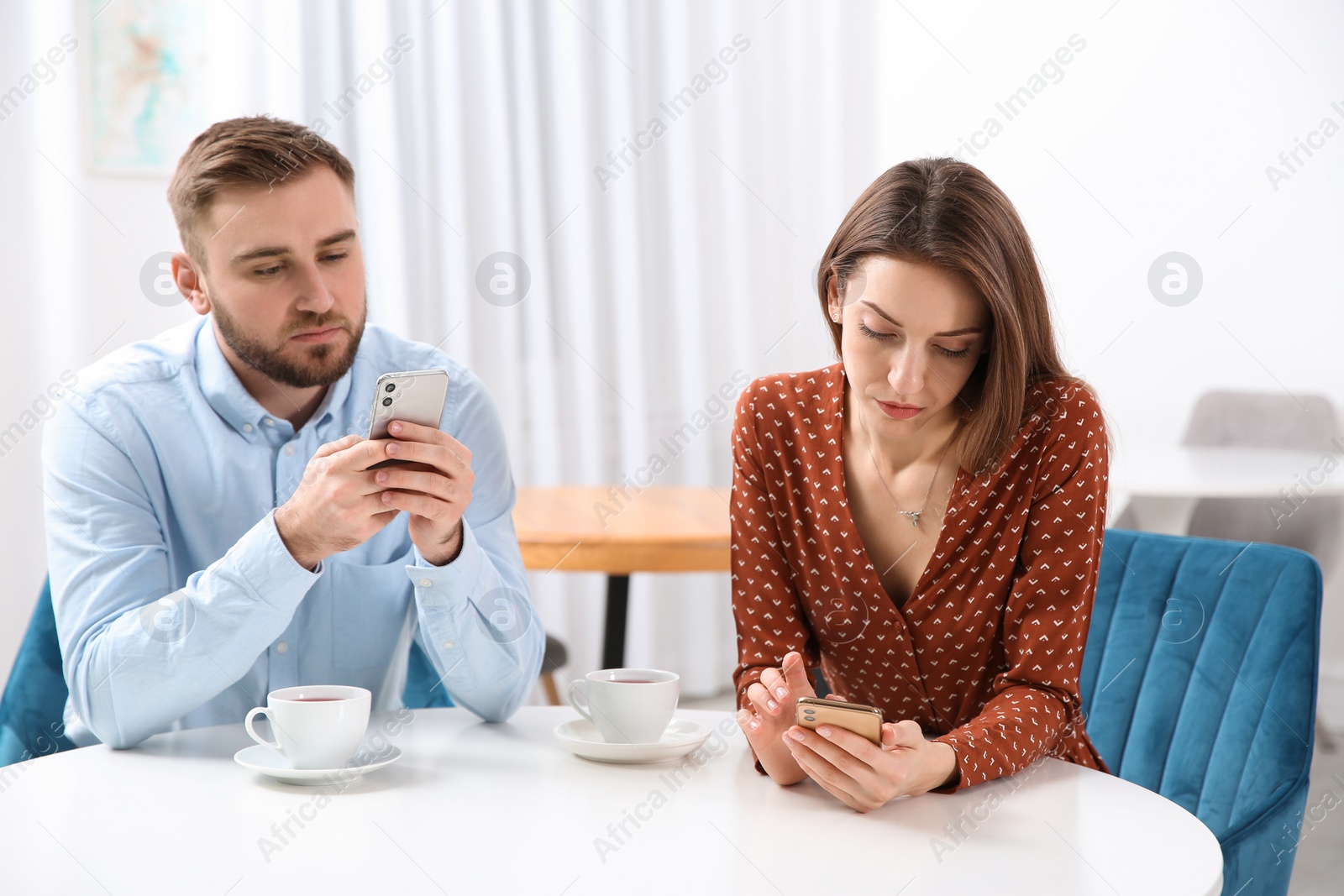 Photo of Couple addicted to smartphones ignoring each other in cafe. Relationship problems