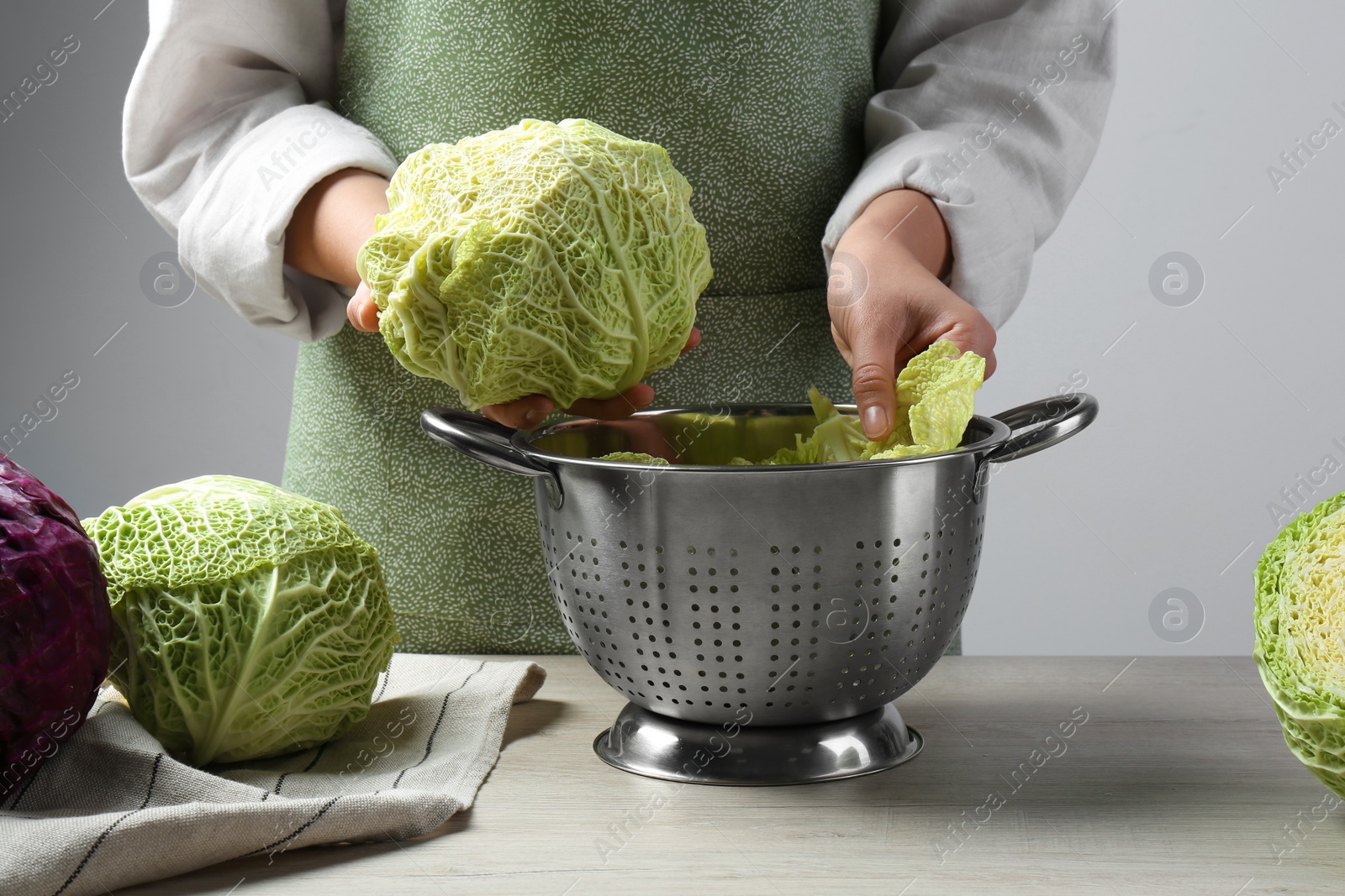 Photo of Woman putting leaf from fresh savoy cabbage at wooden table, closeup