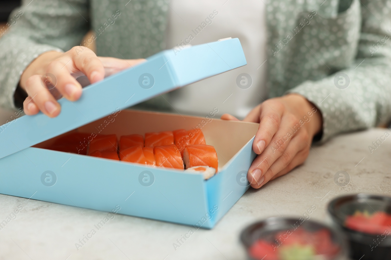 Photo of Woman unpacking her order from sushi restaurant at table in kitchen, closeup