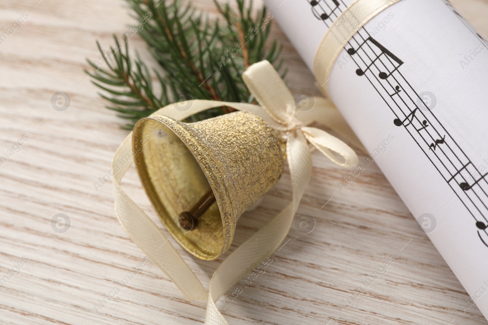 Photo of Golden shiny bell with bow, music sheet and fir twig on wooden table, closeup. Christmas decoration