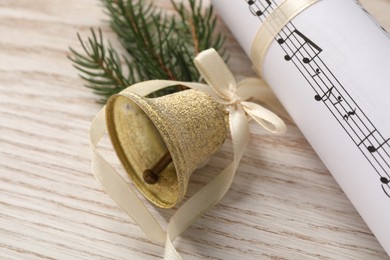 Golden shiny bell with bow, music sheet and fir twig on wooden table, closeup. Christmas decoration