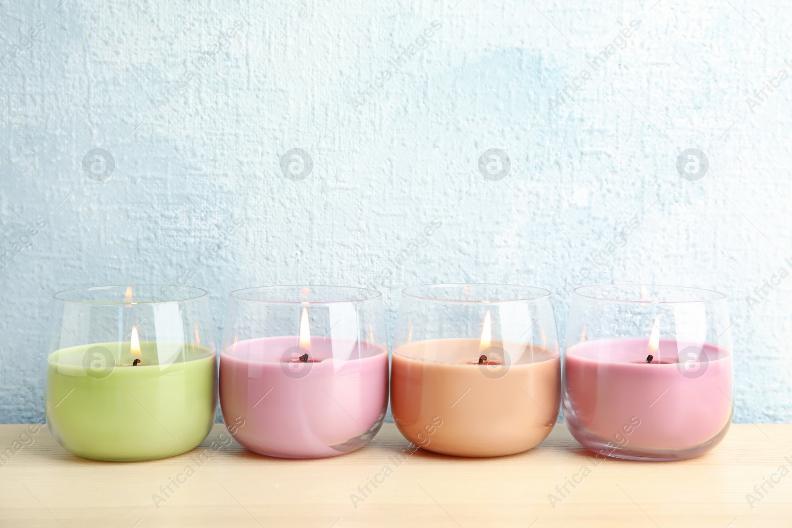 Photo of Burning wax candles in glass holders on wooden table, space for text