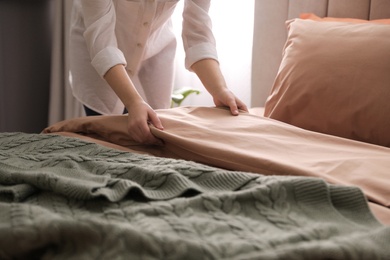 Photo of Woman making bed with stylish linens in room, closeup