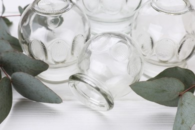 Photo of Glass cups and eucalyptus leaves on white wooden table, closeup. Cupping therapy