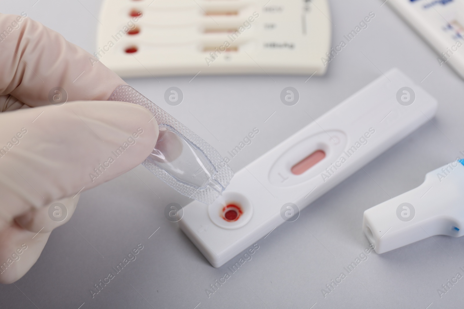 Photo of Doctor dropping buffer solution onto disposable express test cassette on light background, closeup