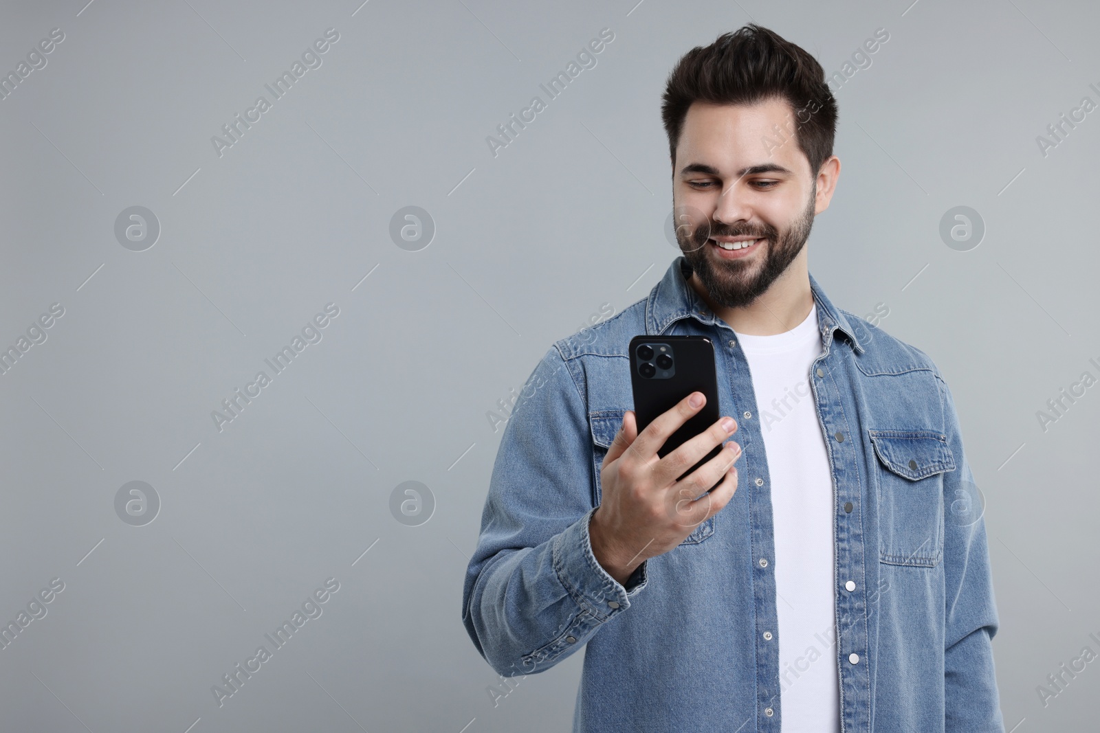 Photo of Happy young man using smartphone on grey background, space for text