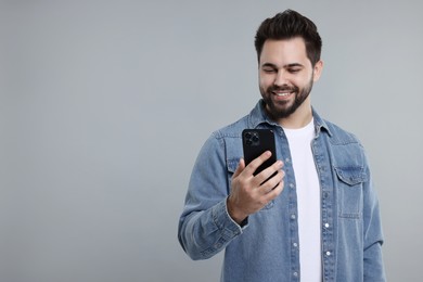 Happy young man using smartphone on grey background, space for text