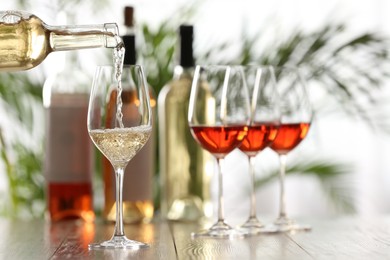 Photo of Pouring white wine from bottle into glass on wooden table, space for text