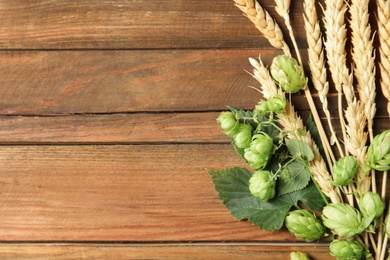 Photo of Fresh green hops and wheat spikes on wooden background, top view with space for text. Beer production
