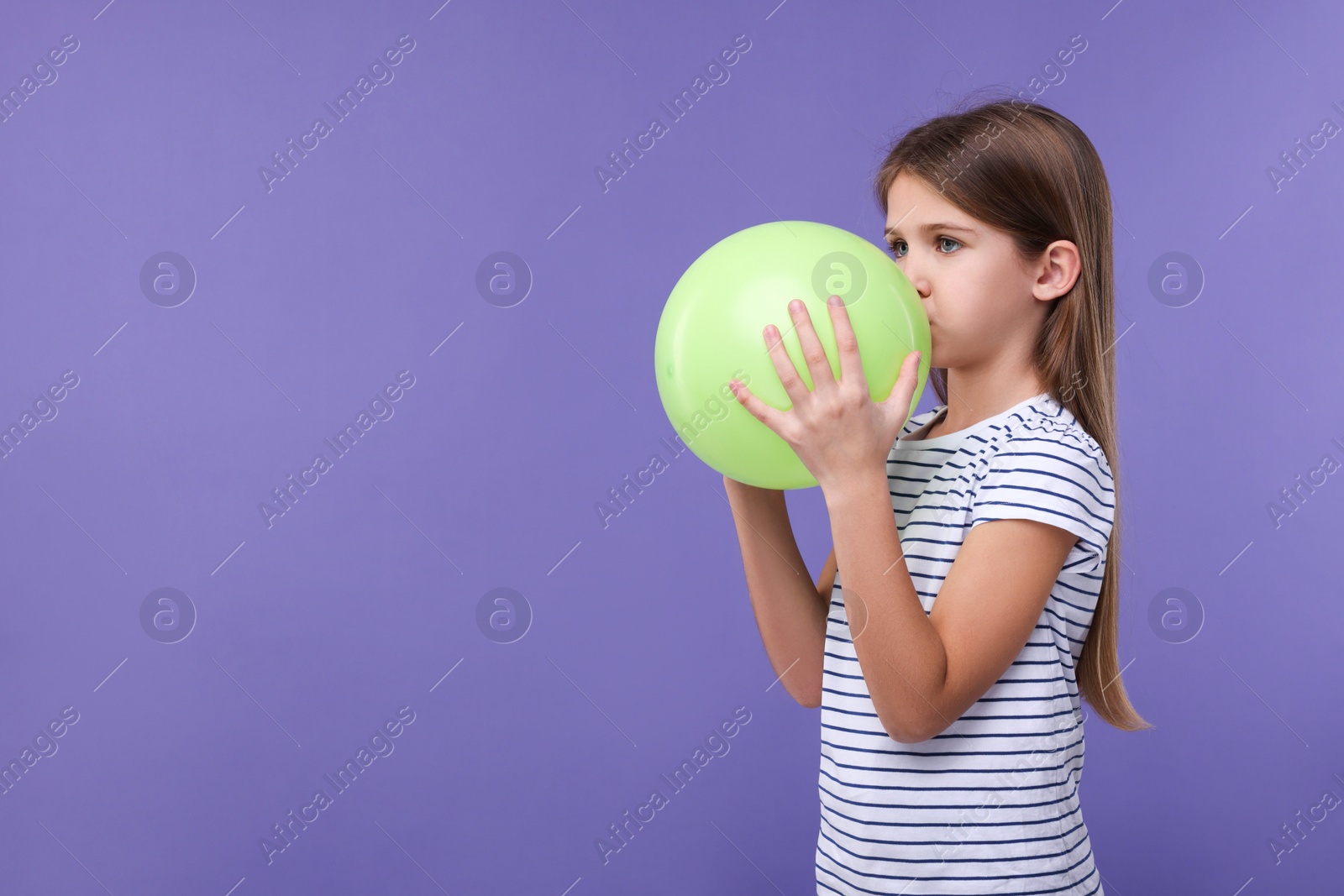 Photo of Girl inflating light green balloon on violet background, space for text